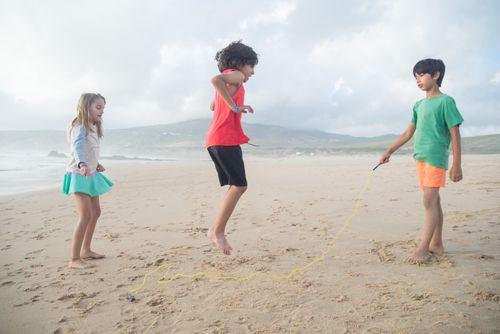 Free Three children enjoy a fun game of jumping rope on a scenic beach in Portugal. Stock Photo