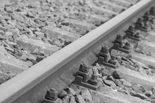 灰色の石による銀の金属の列車の線路の周囲の黒い金属ボルト