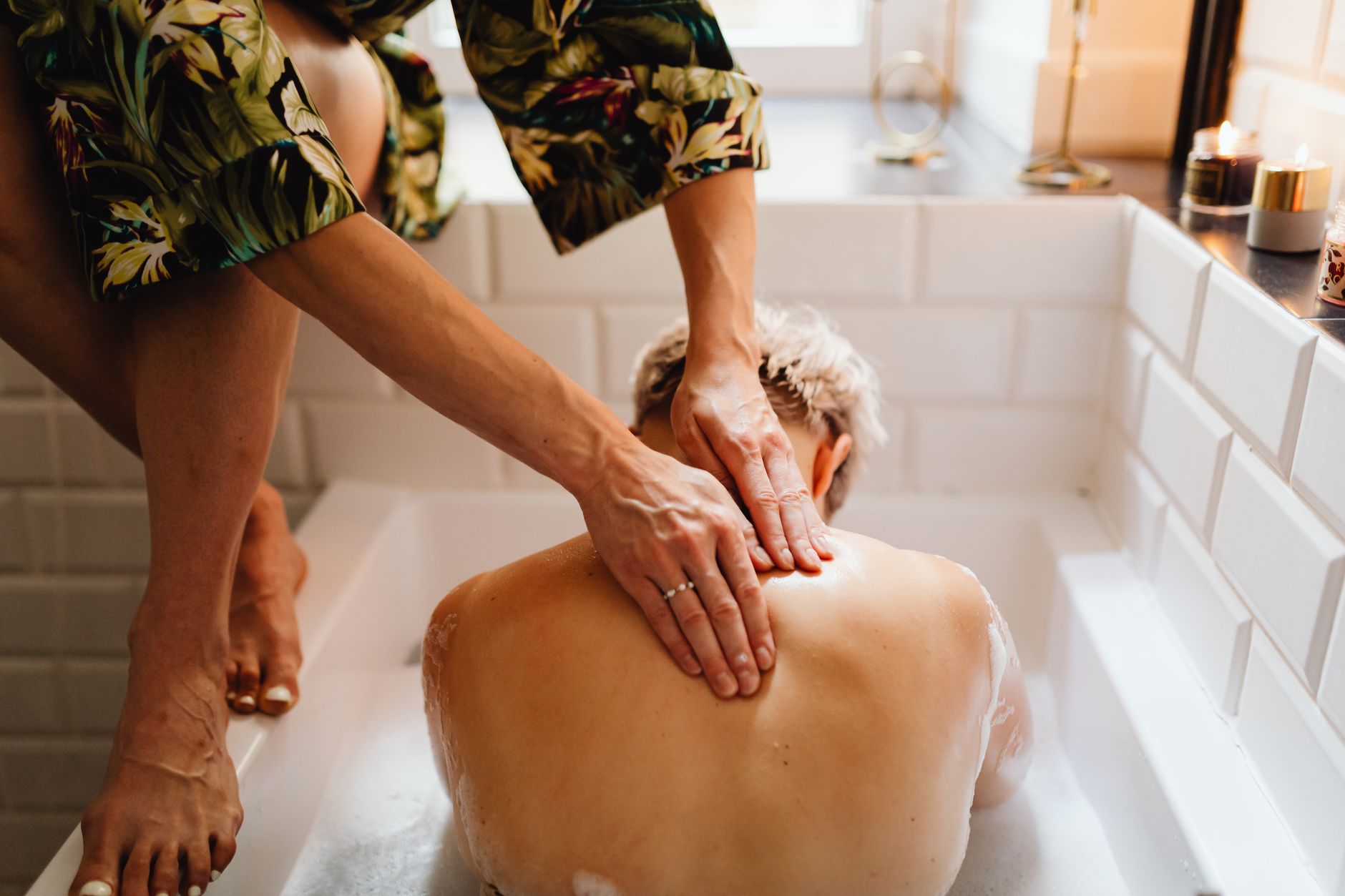 A calming back massage in a bathtub, surrounded by soft lighting and candles, evokes relaxation.