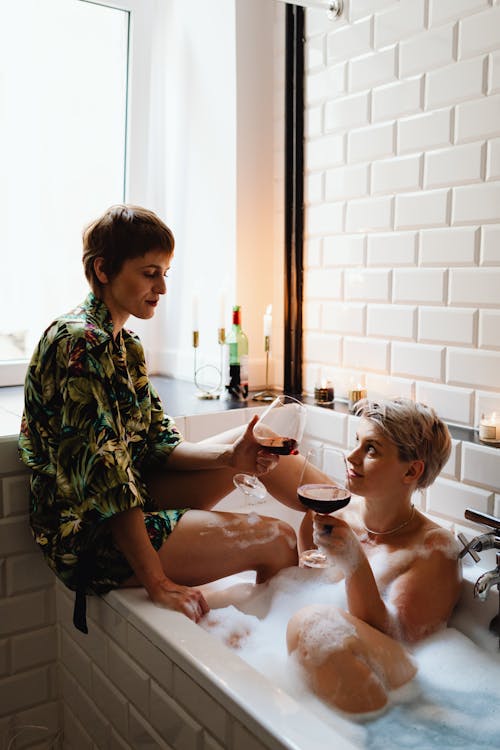 A Couple Holding Wine Glasses While in the Tub
