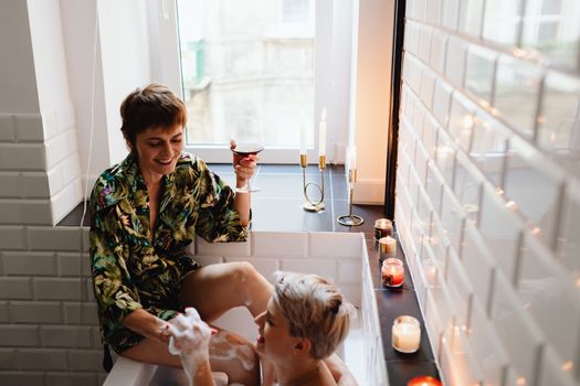 A Woman Sitting on the Rim of a Bathtub Holding a Glass of Wine