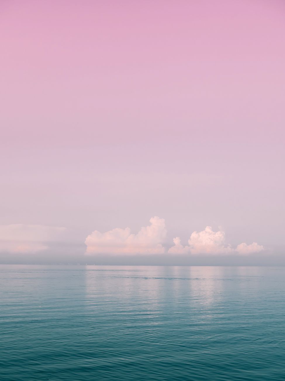Serene ocean view with pink sky and soft clouds at sunset, perfect for calm and peaceful moods.