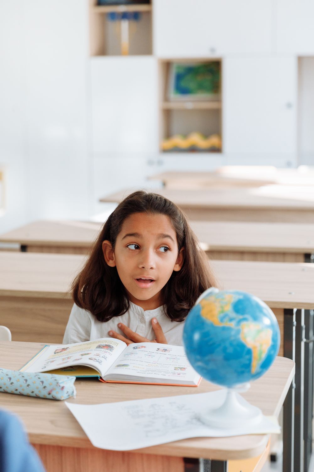 A schoolgirl studying with a globe on her classroom desk