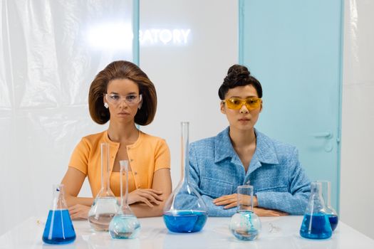Two scientists in a laboratory analyzing blue liquid in flasks wearing protective goggles.