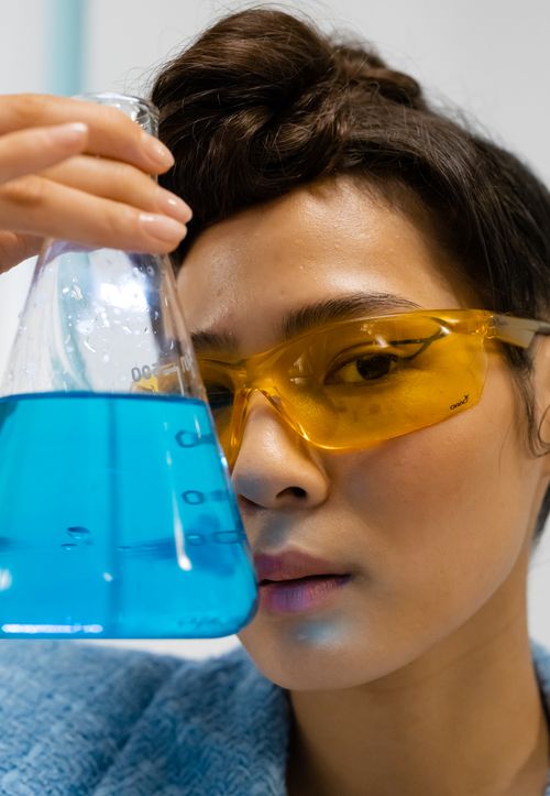 Free Female scientist examining a blue liquid in a laboratory flask, showcasing scientific research. Stock Photo