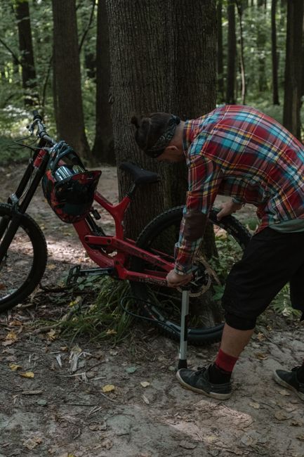 A man in plaid shirt repairing his mountain bike in a lush forest setting during summer.