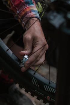 Detailed view of a hand using a tool to adjust bicycle spokes in an outdoor setting.