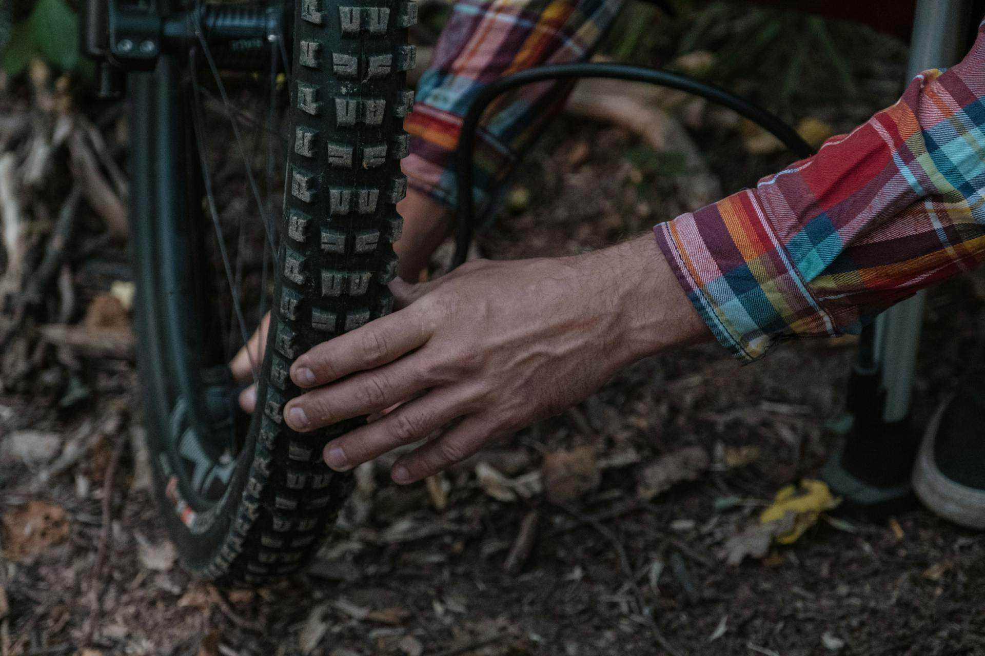 Person in plaid shirt inflating a mountain bike tire in a natural setting, highlighting maintenance and adventure.