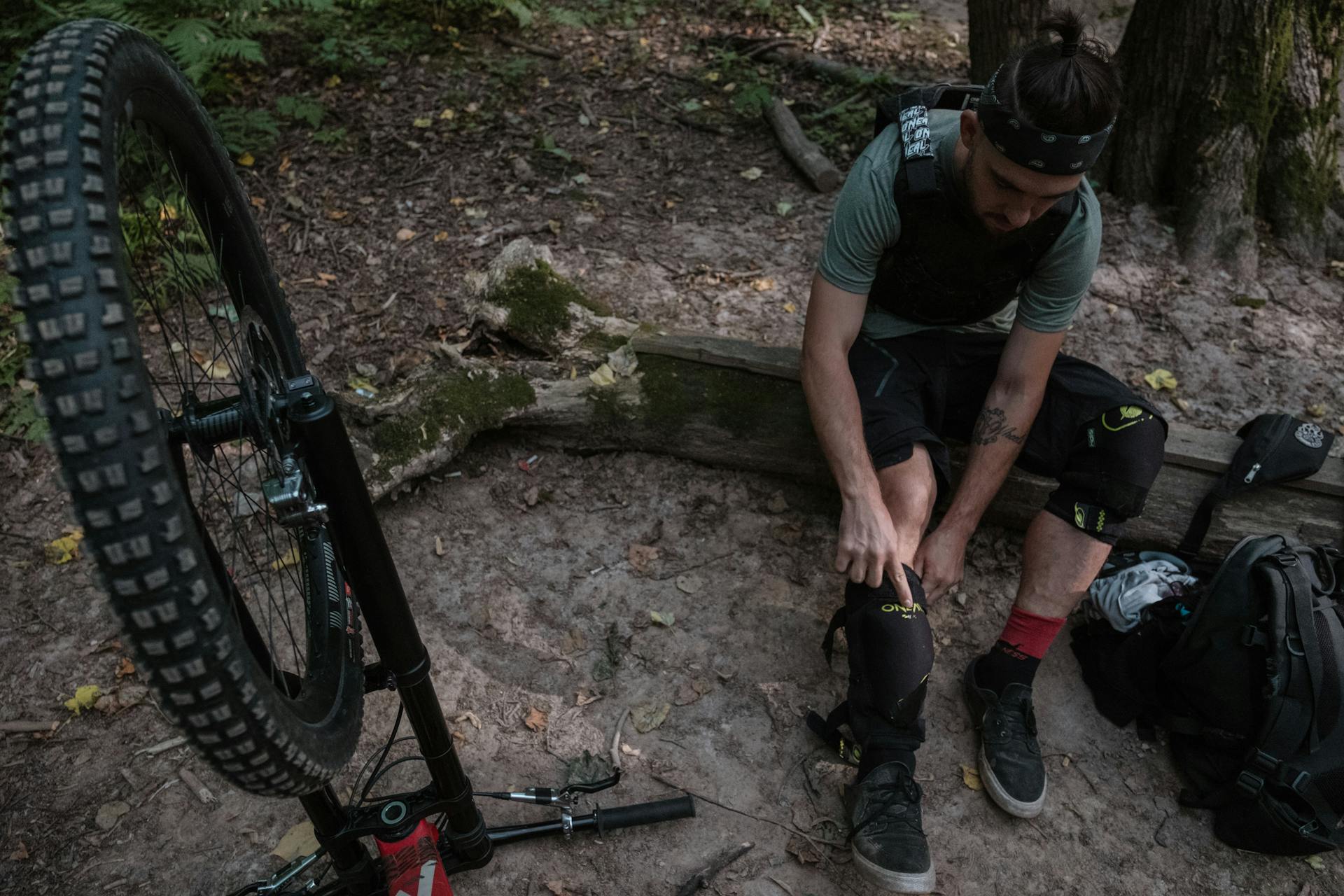 A man prepares for downhill mountain biking in a forest, wearing protective gear.