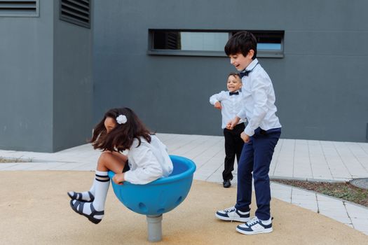 Three children in formal attire enjoy playful moments at a modern outdoor playground.