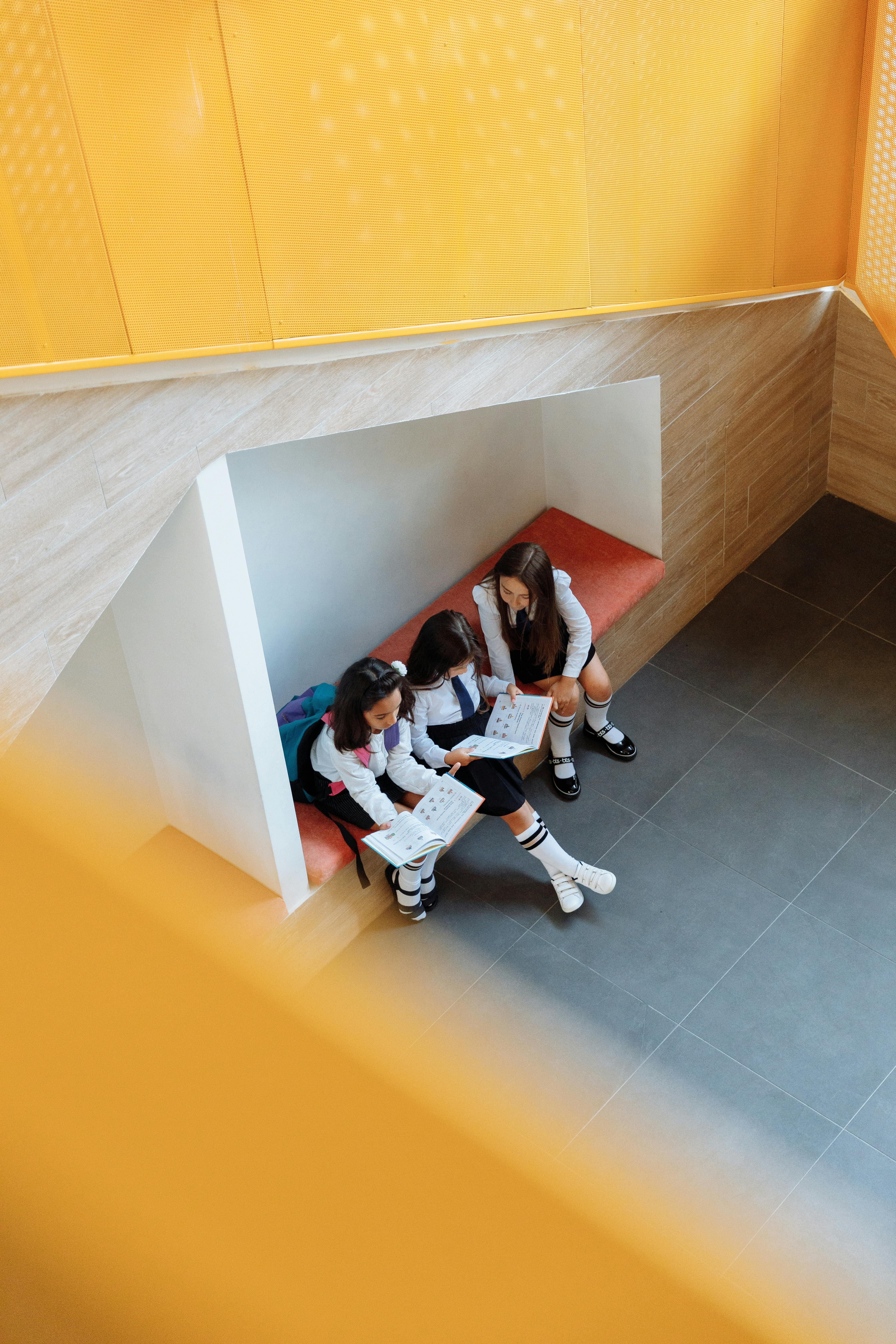 Free Three girls reading books together in a modern, bright classroom setting. High angle view. Stock Photo