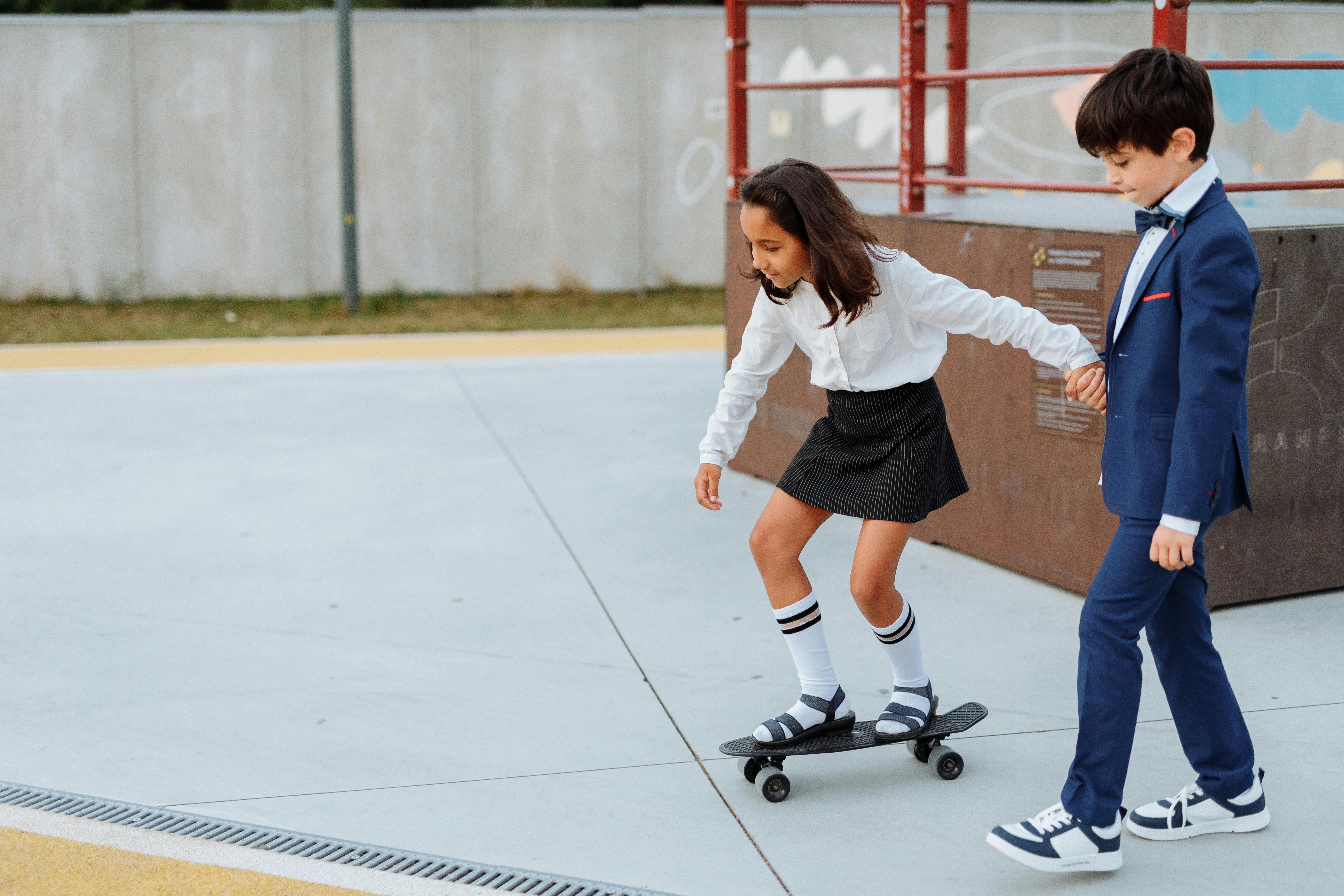 girl holding the hand of a boy while riding a penny board