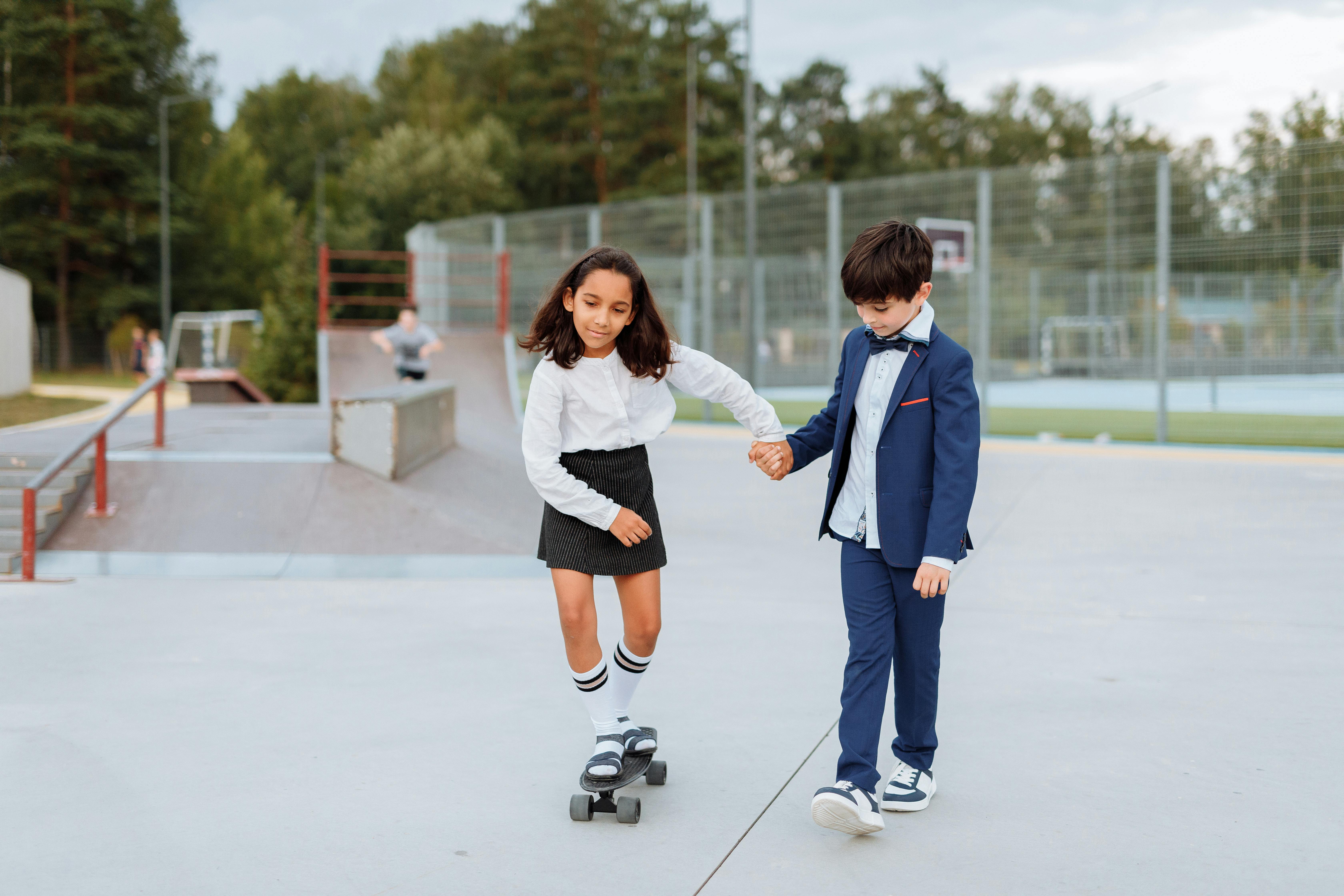 girl holding the hand of a boy while riding a penny board