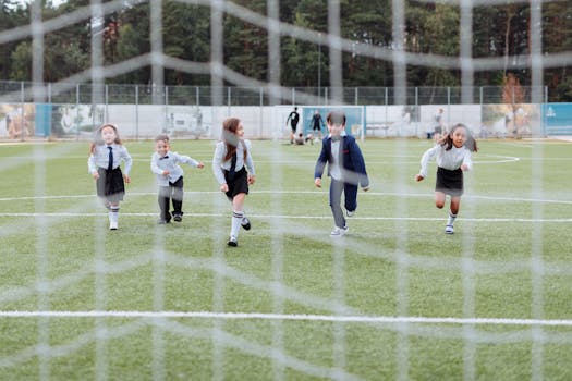 Group of children in uniforms playing soccer during daytime on a grass field.