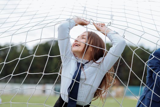 A joyful girl in a school uniform playing in a soccer net outdoors, expressing happiness.