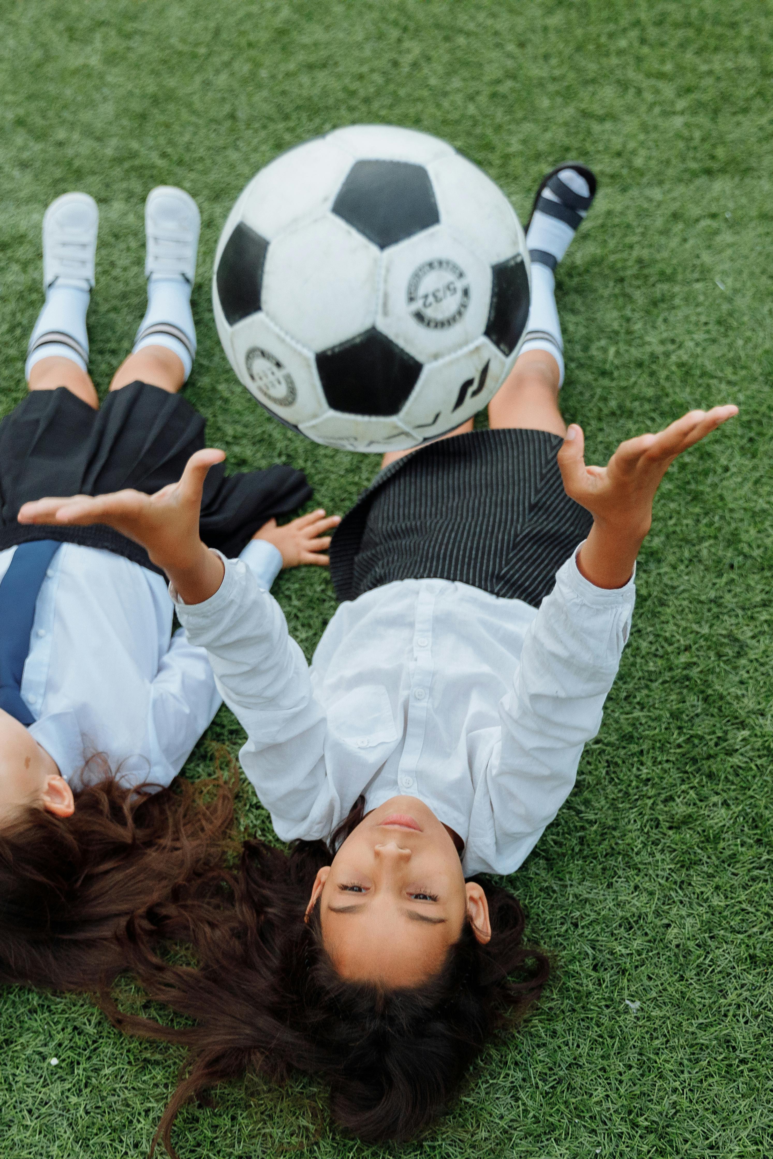 high angle shot of a girl throwing a soccer ball while lying down on the grass