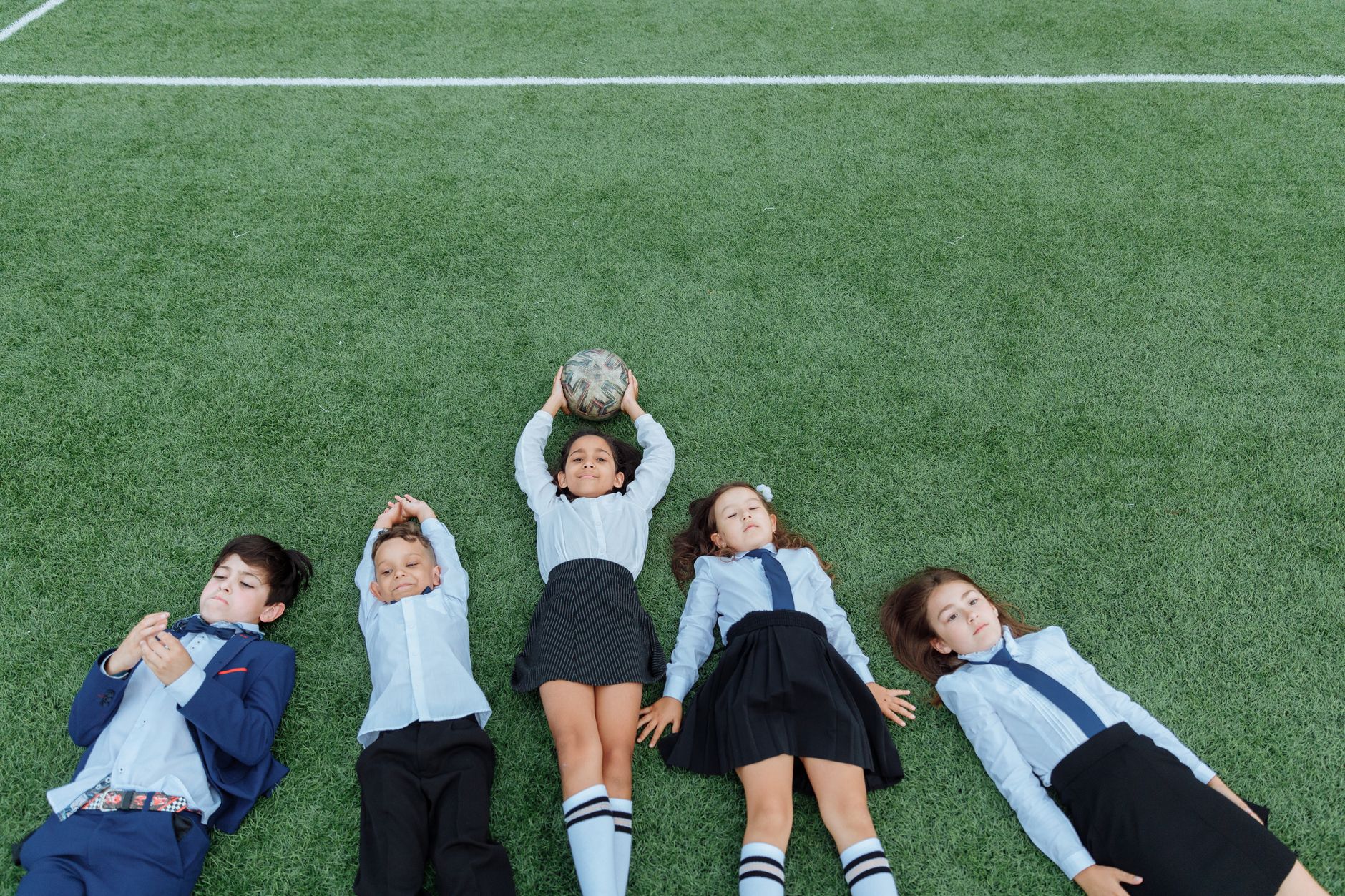 French school fete Cairo — Group of children in uniforms lying on a soccer field with a ball.