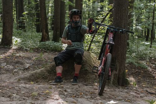 Free A mountain biker in protective gear rests on a forest trail, showcasing outdoor adventure. Stock Photo