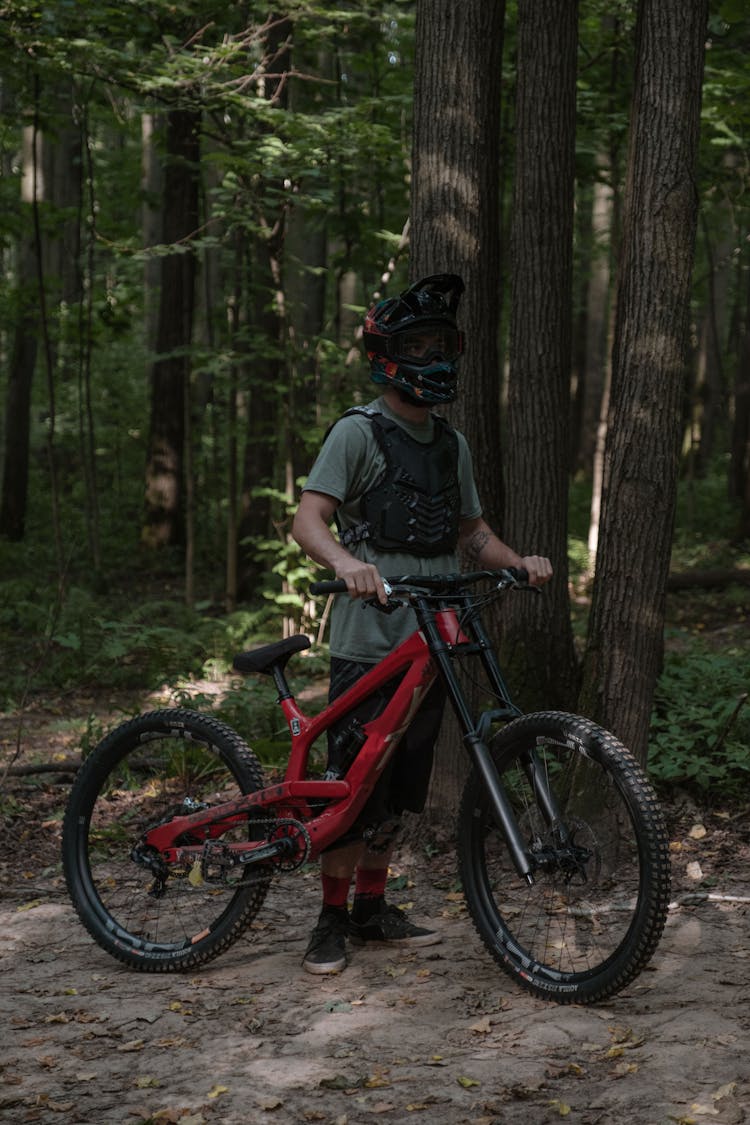 A Man Standing Near The Trees Holding His Bike 