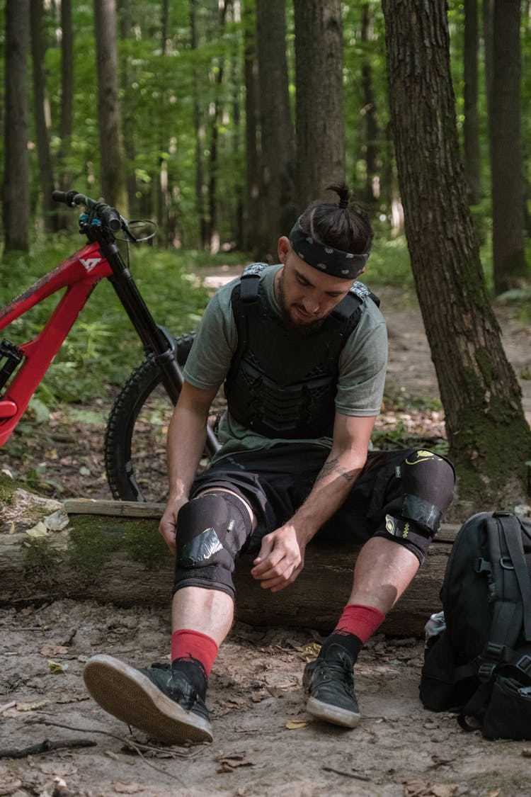 Man Sitting On A Tree Log Looking At His Knee Pad