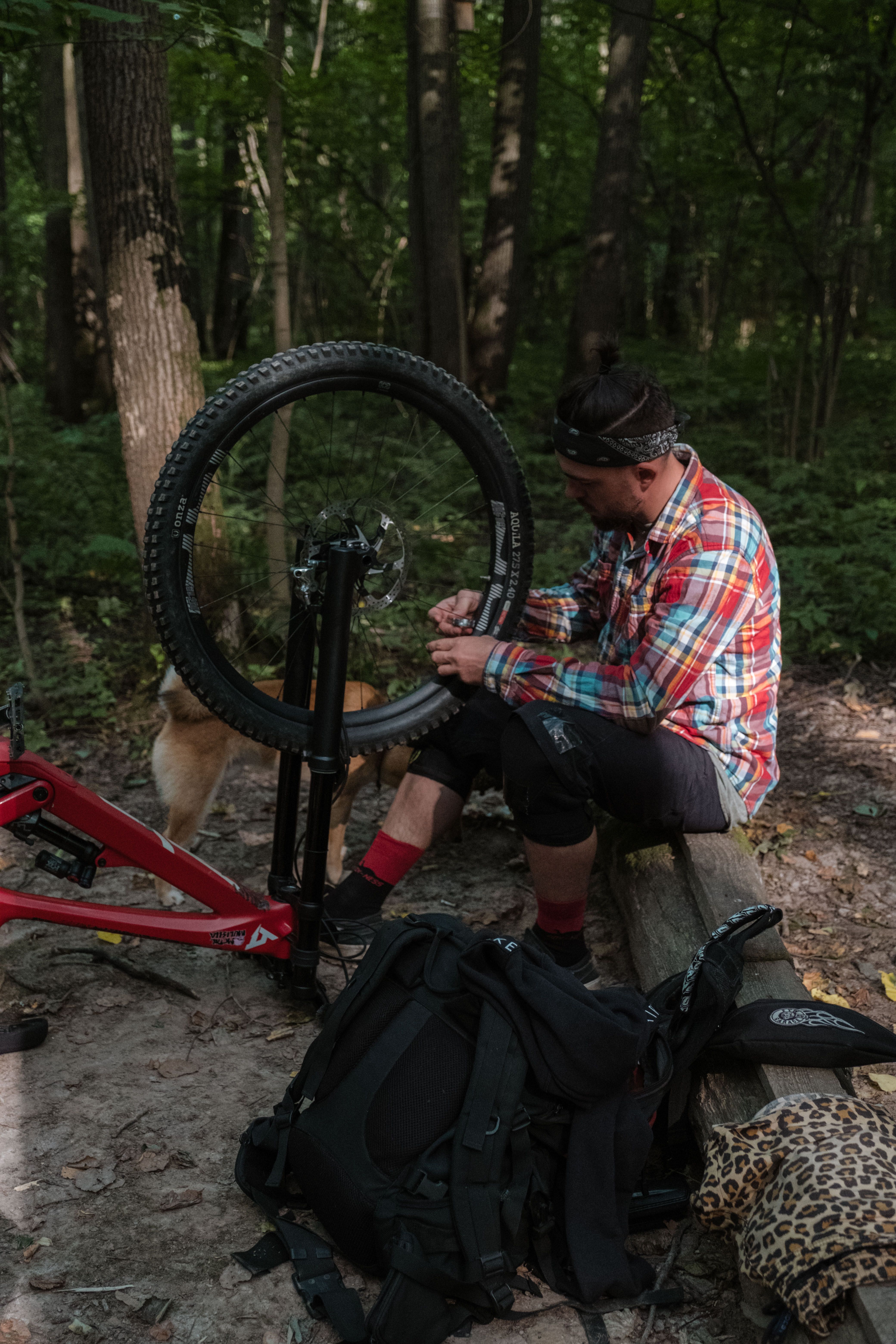 Man fixing a mountain bike tire in a wooded area, surrounded by trees.