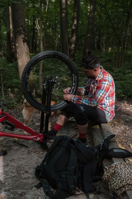 Man fixing a mountain bike tire in a wooded area, surrounded by trees.