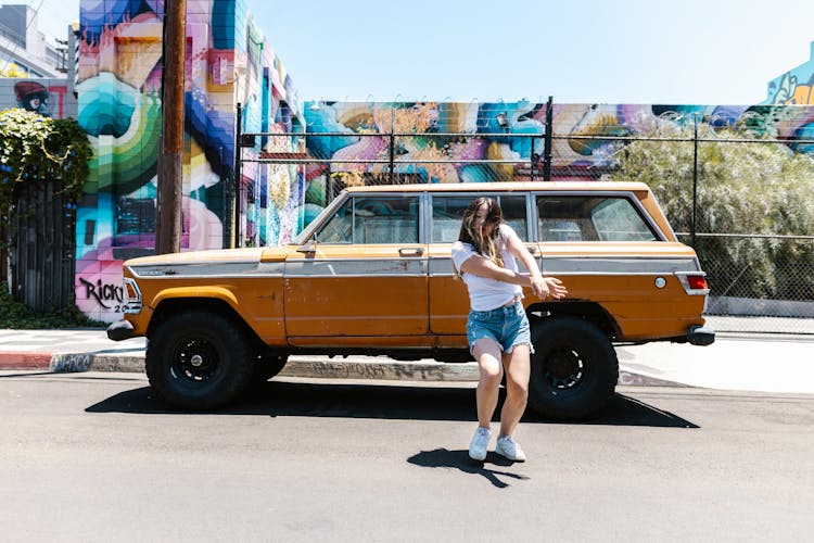 Woman In A White Shirt Dancing Near A Brown Car