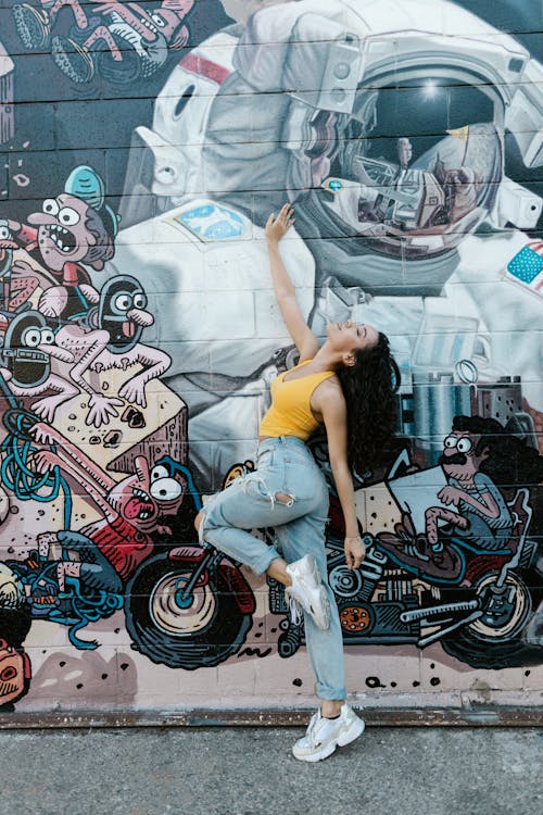 Photo of a Woman in a Yellow Top Beside a Wall with Graffiti