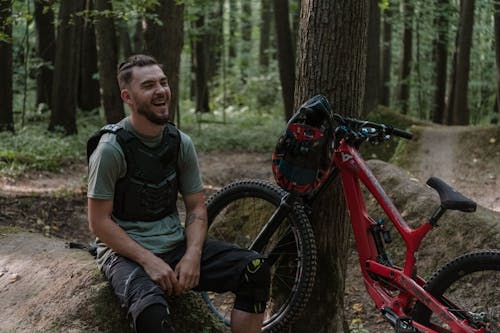 A Biker Laughing while Sitting by a Tree
