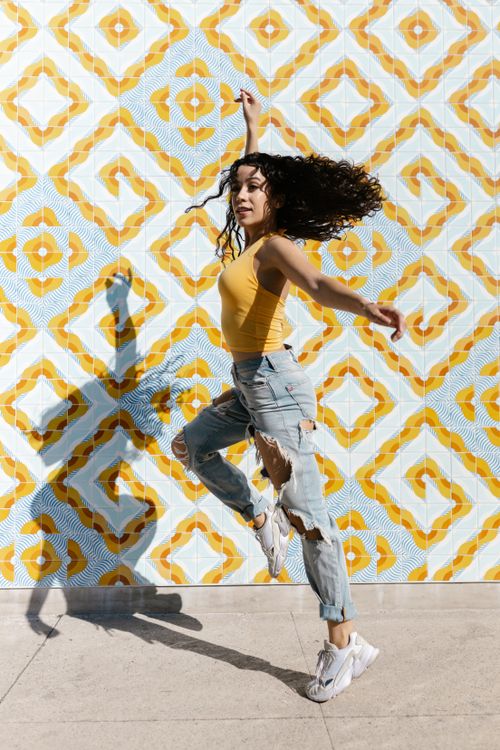 Free Woman performing a dynamic street dance against a vibrant geometric wall in urban setting. Stock Photo