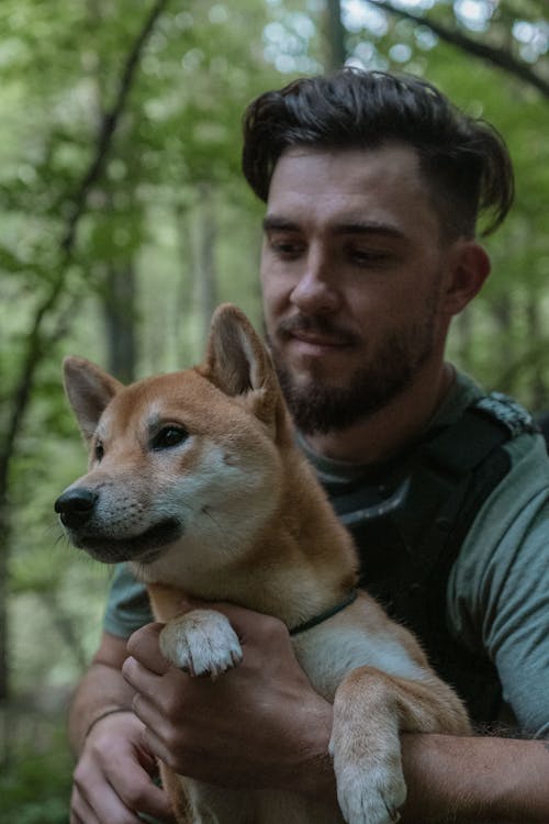 Photo of a Man in a Green Shirt Carrying His Shiba Inu Dog