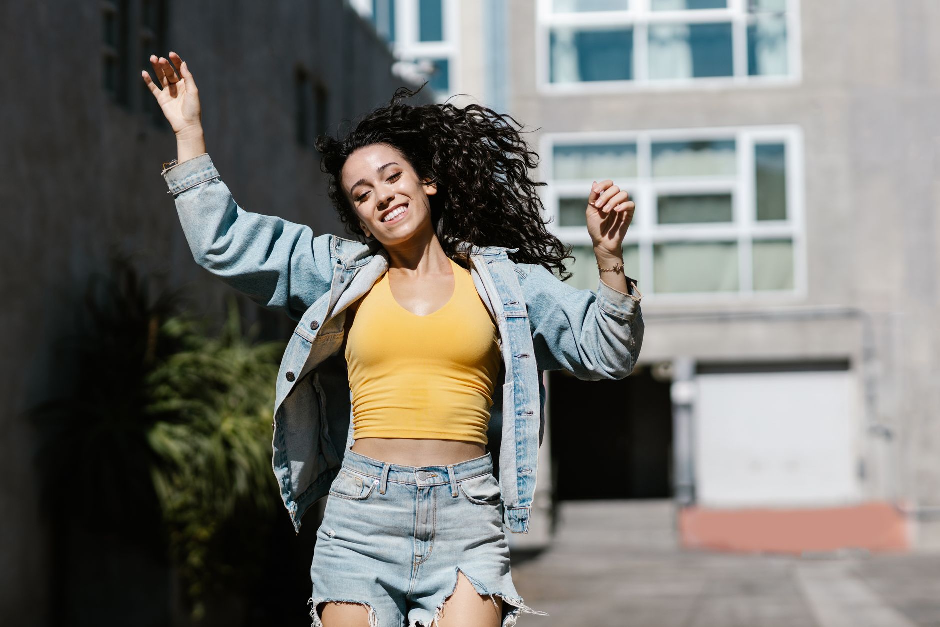 Young woman joyfully posing outdoors in denim and yellow. Vibrant and energetic scene.
