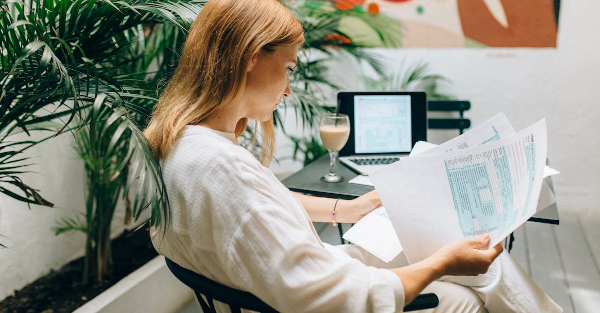 Photo by Nataliya Vaitkevich A woman reviews financial documents in an indoor garden space, with a laptop open.