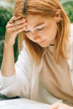 A woman appears stressed while reviewing papers outside, reflecting on financial concerns.