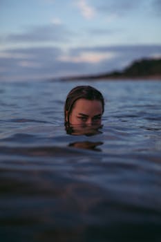 A mysterious portrait of a woman partially submerged in the calm sea during twilight.