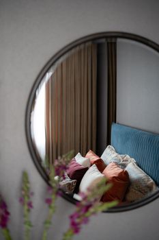 Stylish bedroom decor reflected in a round mirror with vibrant throw pillows.