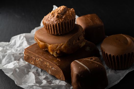 Indulgent assortment of chocolates and fudge on paper with dark backdrop.