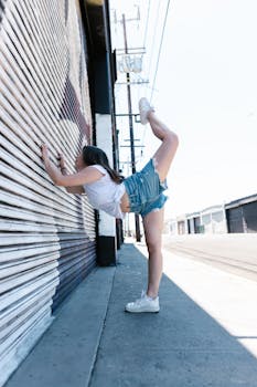 A young woman performs a flexible pose on an urban sidewalk, showcasing strength and balance.