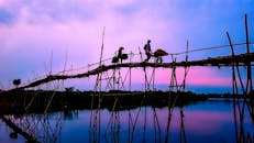 黄昏时分，一个骑自行车的人穿过竹桥，身影倒映在平静的河水中