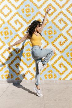 Stylish woman in a yellow tank top dancing against a bold geometric wall.