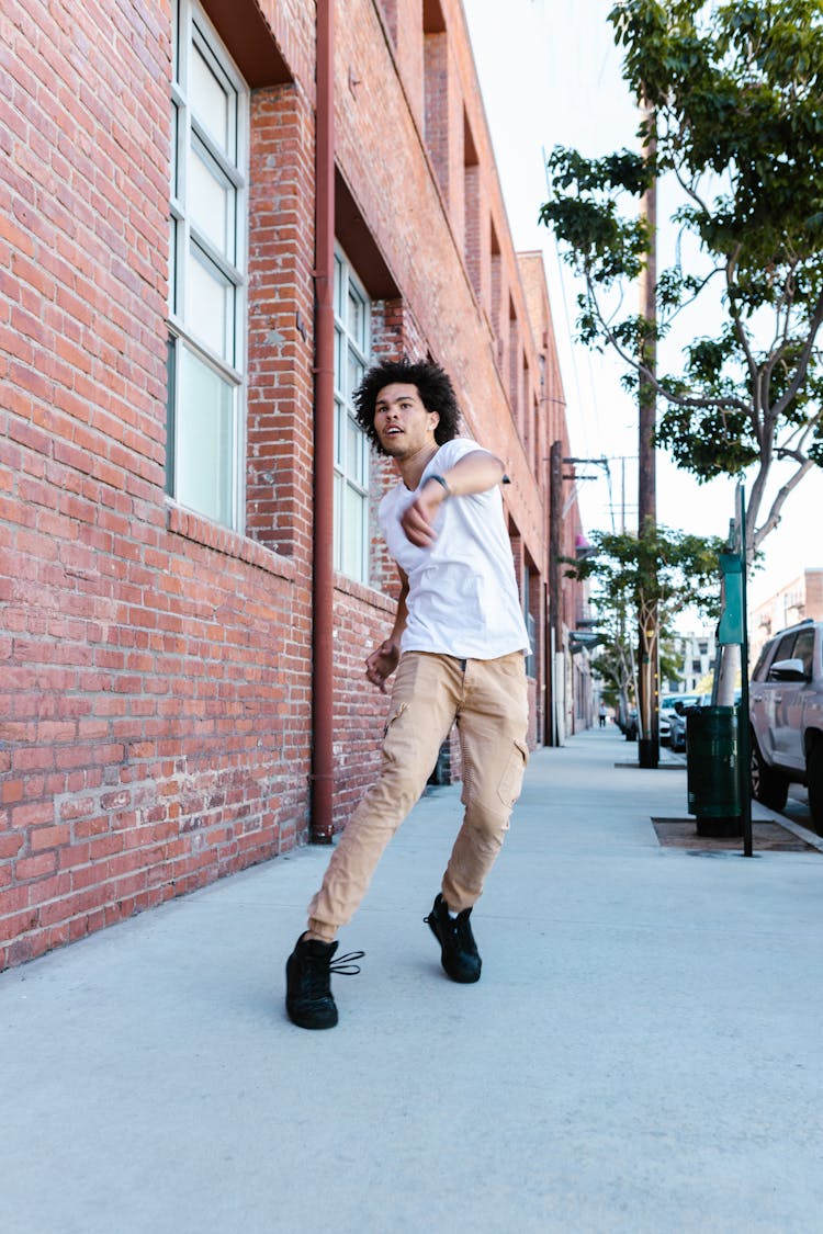 A Man In A White Shirt And Khaki Pants Dancing On A Sidewalk