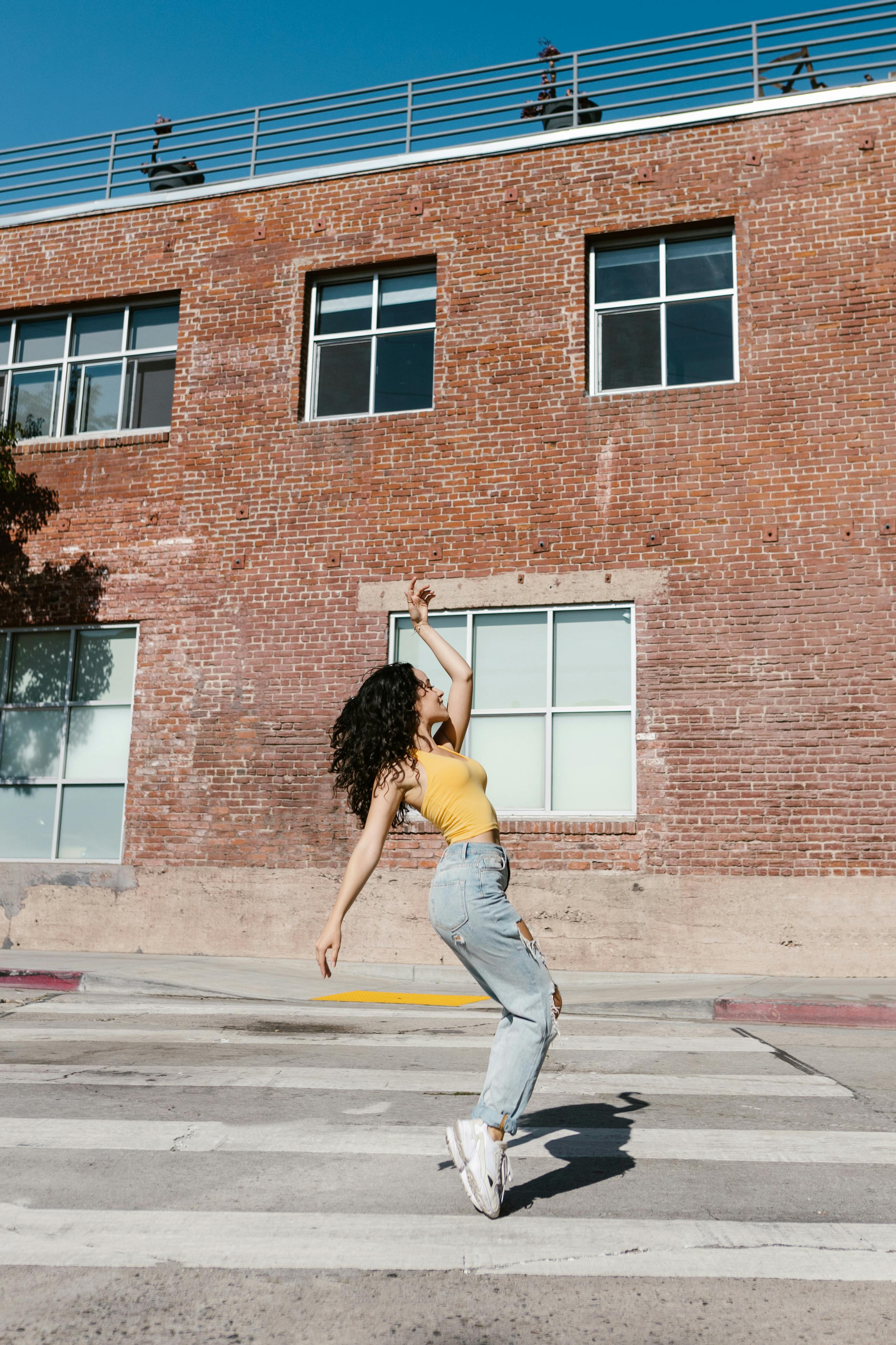 a woman in yellow tank top and denim jeans dancing on the street