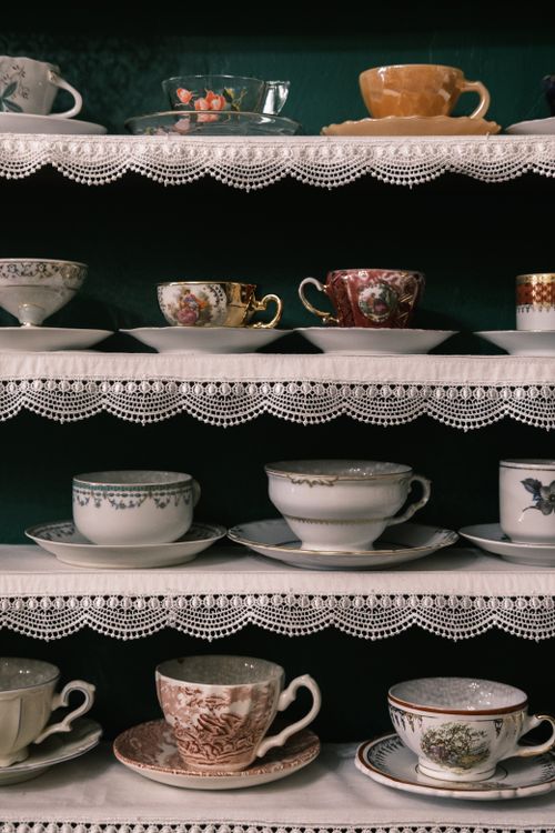 Free A beautiful assortment of porcelain teacups and saucers, artistically arranged on lace-trimmed shelves. Stock Photo