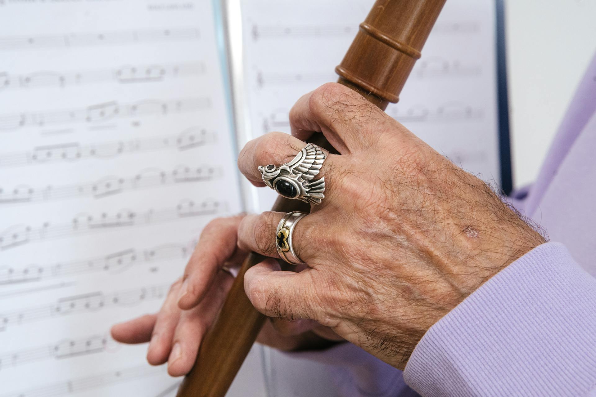 Detailed shot of hands with rings playing a wooden flute, with sheet music in the background.