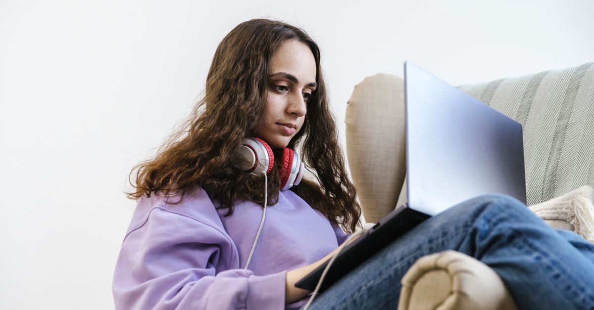 A student in a dorm room working on a laptop with music posters on the wall