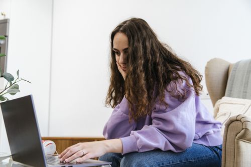 Free A young woman focusing on her laptop while sitting on an armchair indoors. Stock Photo