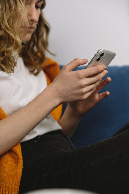 Free A woman sitting on a couch indoors, focused on her smartphone, wearing casual attire. Stock Photo