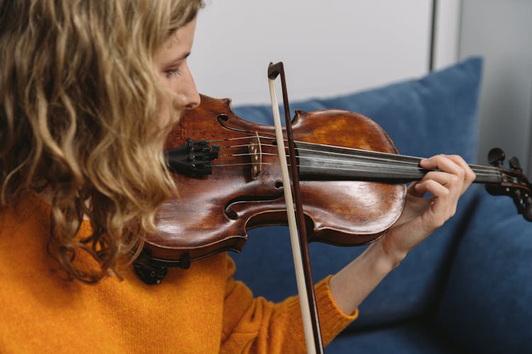 A Woman In An Orange Sweater Playing The Violin