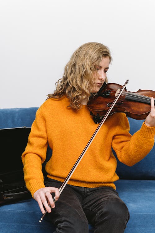 Free A Woman in a Yellow Sweater Playing the Violin on a Couch Stock Photo