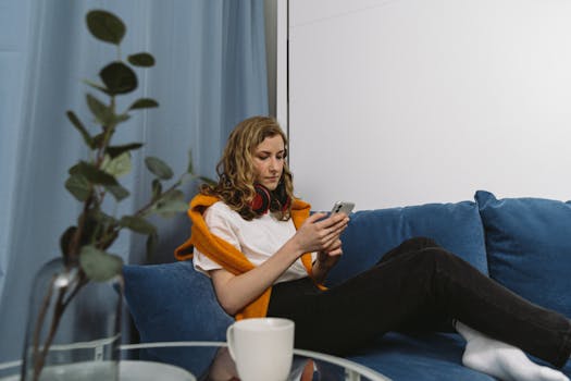 A woman sitting on a blue sofa using a smartphone, with a modern home setting.